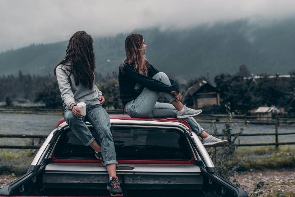 На фото две девушки сидят на кузове авто.