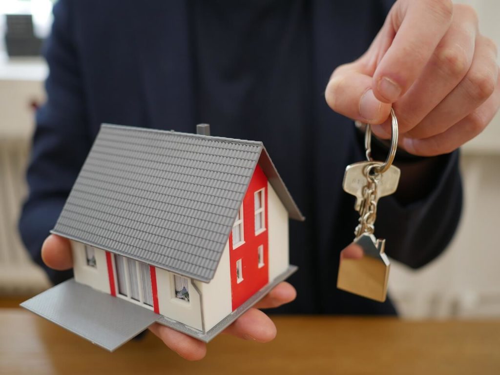 На фото изображен мужчина с ключами и макетом дома в руках.