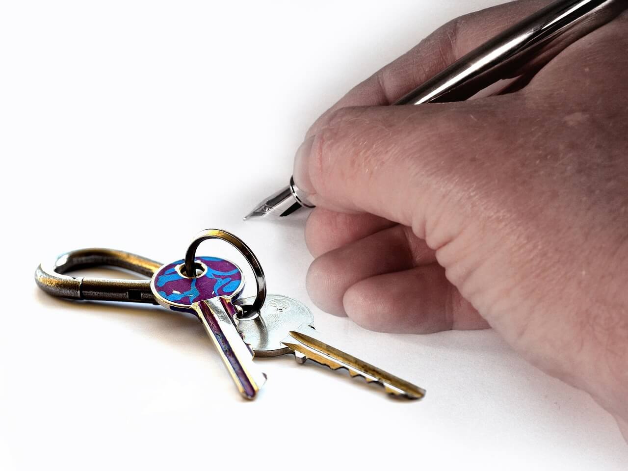 На фото мужчина подписывает договор на котором лежит связка ключей.