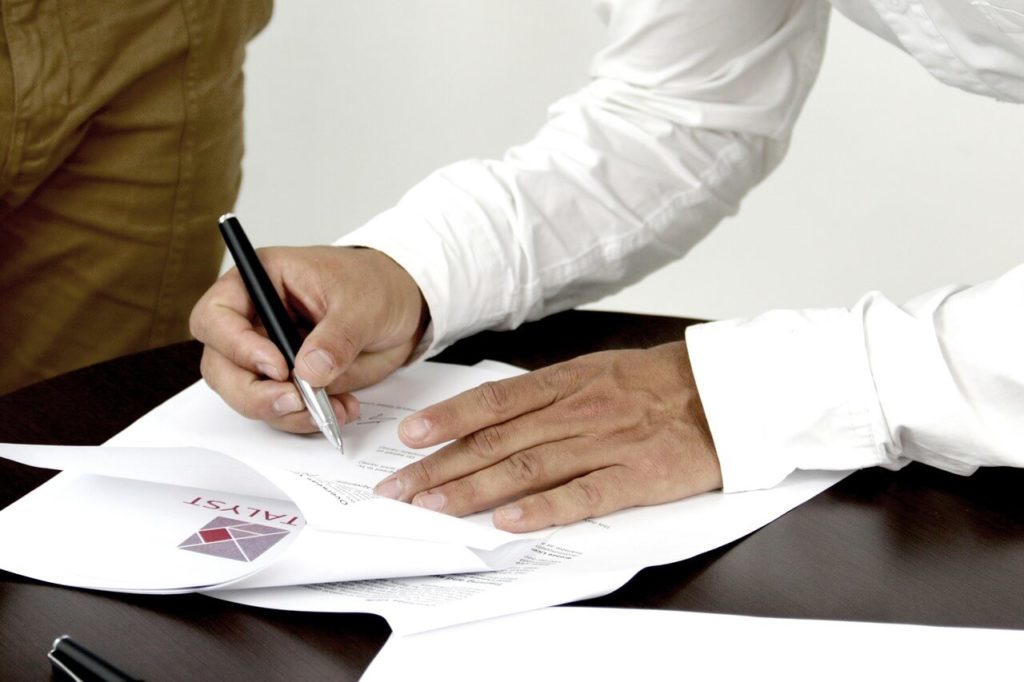 На фото мужчина подписывает документ.